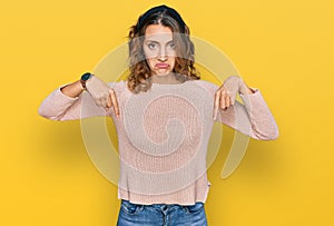 Beautiful young caucasian woman wearing casual sweater pointing down looking sad and upset, indicating direction with fingers,
