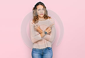 Beautiful young caucasian woman wearing casual sweater pointing to both sides with fingers, different direction disagree