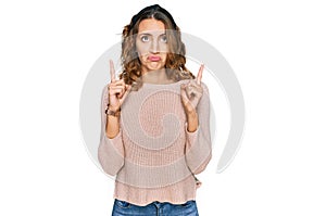 Beautiful young caucasian woman wearing casual sweater pointing up looking sad and upset, indicating direction with fingers,