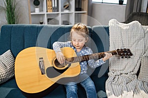 Beautiful young charming little girl smiling while playing classic guitar at home.