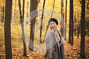 Beautiful young cheerful european woman wearing beret and coat walking in autumn forest