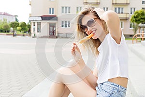 Beautiful young cheerful happy girl eating ice cream , smiling in shorts and a white T-shirt on the area on a bright sunny day