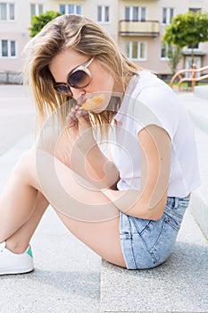 Beautiful young cheerful happy girl eating ice cream , smiling in shorts and a white T-shirt on the area on a bright sunny day