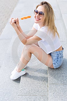 Beautiful young cheerful happy girl eating ice cream , smiling in shorts and a white T-shirt on the area on a bright sunny day