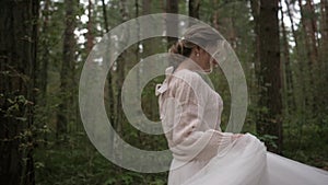 A beautiful young cheerful and joyful bride in a wedding dress and a delicate sweater runs and spins in the forest. Slow