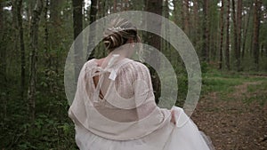 A beautiful young cheerful and joyful bride in a wedding dress and a delicate sweater runs and spins in the forest. Slow