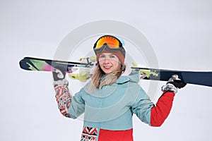 A beautiful young chew in an extreme sports suit, a hat and a helmet with a mask on the winter slope is holding alpine