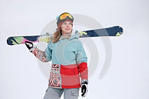 A beautiful young chew in an extreme sports suit, a hat and a helmet with a mask on the winter slope is holding alpine