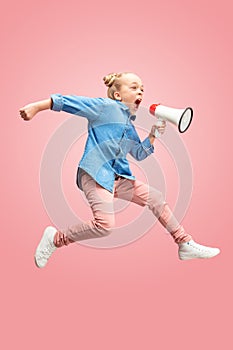 Beautiful young child teen girl jumping with megaphone isolated over pink background