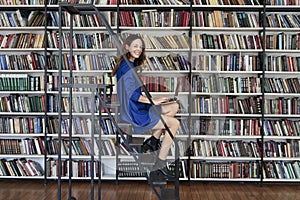 Beautiful young college student sitting on stairs in the library, working on laptop.