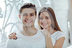 Beautiful young couple in bedroom is sitting on bed, smiling and looking at camera. Celebrating Saint Valentine`s Day