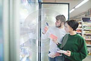 A beautiful young couple chooses frozen foods near the refrigerator in a supermarket