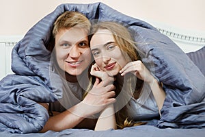 Beautiful young couple cuddling in bed under the covers