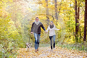 Beautiful young couple with dog running in autumn forest