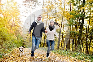 Beautiful young couple with dog running in autumn forest