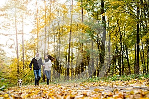 Beautiful young couple with dog running in autumn forest