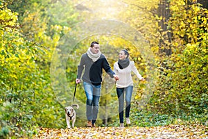 Beautiful young couple with dog running in autumn forest