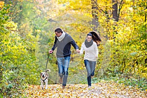 Beautiful young couple with dog running in autumn forest