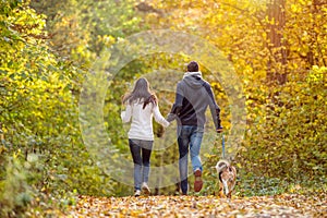 Beautiful young couple with dog running in autumn forest