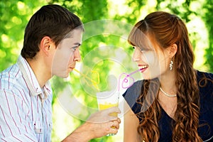 Beautiful Young Couple Drinking Juice from one Glass with Colored Tubes. Picnic in Countryside. Happy Family Outdoor. Smiling Man