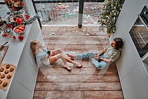 Beautiful young couple drinking wine while sitting on the kitchen floor at home. Top view