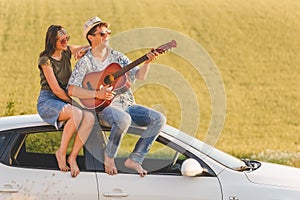 Beautiful young couple enjoying on car roof against yellow field background.
