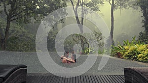 Beautiful young couple enjoying together in infiniti pool overlooking tropical misty jungle view during rain