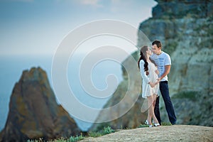 Beautiful young couple expecting baby posing on mountain view with blue sea as background