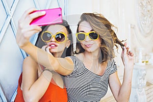 Beautiful young couple fashionable girls blonde and brunette in a bright yellow dress and sunglasses posing and smiling for the ca