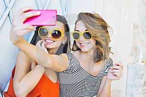 Beautiful young couple fashionable girls blonde and brunette in a bright yellow dress and sunglasses posing and smiling for the ca