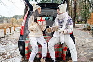 Young couple giving presents and looking each other sitting in the trunk in winter holidays.