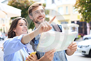 Beautiful young couple holding a map and smiling while standing outdoors.