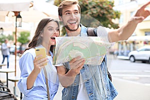 Beautiful young couple holding a map and smiling while standing outdoors