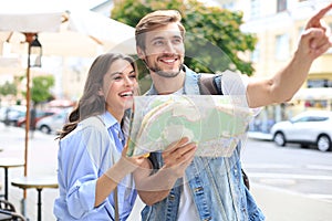 Beautiful young couple holding a map and smiling while standing outdoors