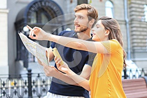 Beautiful young couple holding a map and smiling while standing outdoors