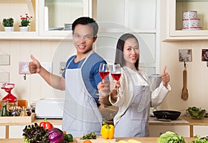 Beautiful young couple is holding wine and thumbs up while cooking in kitchen at home