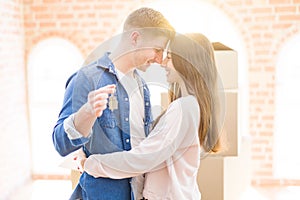 Beautiful young couple hugging in love and showing keys of new house, smiling happy moving to a new apartment