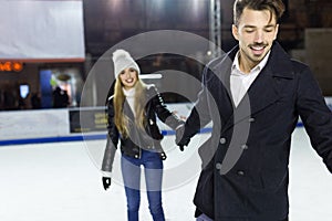 Beautiful young couple ice skating on rink outdoors.