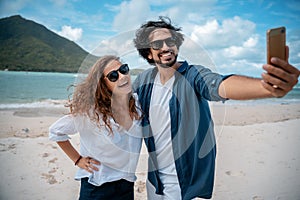 Beautiful young couple joyfully on the white sand making selfie on a smartphone. Honeymoon Travel and Vacation on the Tropical