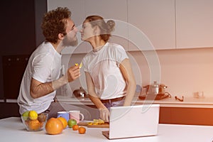 Beautiful young couple kissing feeding each other making fun at modern kitchen and smiling while cooking at home. Pretty