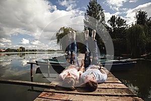 Beautiful young couple lies on a wooden bridge on the lake, looks lovingly at each other and smiles. Love story