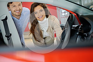 Beautiful young couple looking a new car at the dealership showroom.