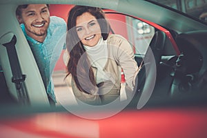 Beautiful young couple looking a new car at the dealership showroom.