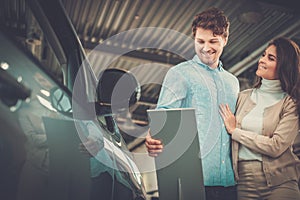 Beautiful young couple looking a new car at the dealership showroom.