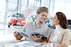 Beautiful young couple looking a new car at the dealership showroom. photo