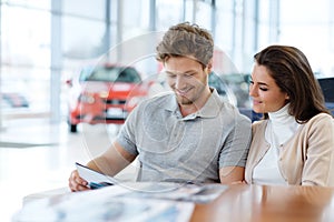 Beautiful young couple looking a new car at the dealership showroom.