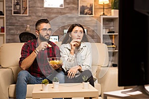 Beautiful young couple looking worried at tv while watching a movie