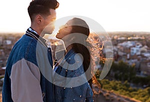 Beautiful young couple in love standing at a building rooftop at the sunset.