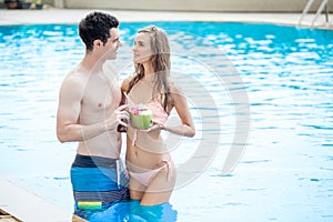 beautiful young couple in love together in swimming pool and drinking cocktails