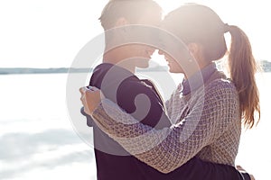 Beautiful young couple in love walking on the shore of the lake at sunset in the rays of bright light